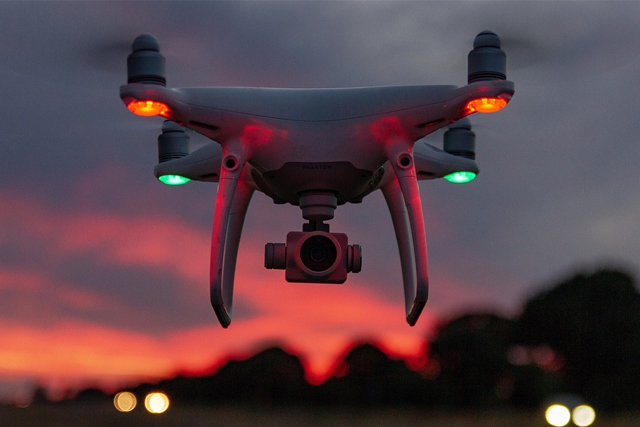 A drone with lights hovering over some countryside.